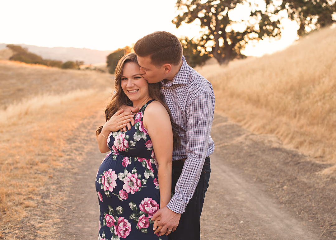 Couple sharing a kiss at golden hour on a hillside path by Alicia Cervenka Photography