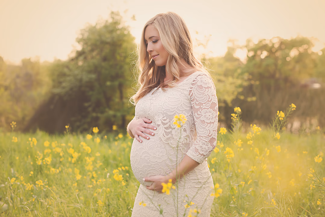 Expectant mother in a lace dress standing in a golden wildflower meadow by Alicia Cervenka Photography